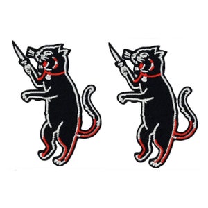 May include: Two black embroidered iron-on patches of a black cat holding a knife. The cat is standing on its hind legs and has a red collar.