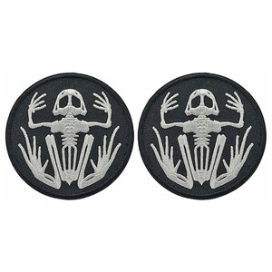 May include: Two black embroidered iron-on patches with a white skeleton frog design.