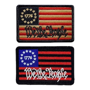 May include: Two embroidered patches featuring the American flag with 13 stars in a circle and the text "We the People". The top patch has a gold and red flag with black text, while the bottom patch has a black and red flag with white text.