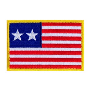 May include: Embroidered patch featuring the American flag design. The patch has a blue square with two white stars in the upper left corner, and red and white stripes. The patch is rectangular with a yellow border.