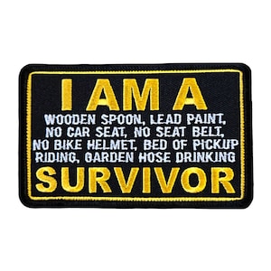 May include: Black embroidered patch with yellow text that reads "I AM A WOODEN SPOON, LEAD PAINT, NO CAR SEAT, NO SEAT BELT, NO BIKE HELMET, BED OF PICKUP RIDING, GARDEN HOSE DRINKING SURVIVOR"