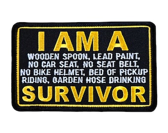 May include: Black embroidered patch with yellow text that reads "I AM A WOODEN SPOON, LEAD PAINT, NO CAR SEAT, NO SEAT BELT, NO BIKE HELMET, BED OF PICKUP RIDING, GARDEN HOSE DRINKING SURVIVOR"