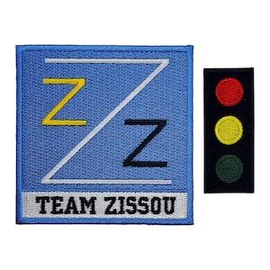 May include: A blue and white embroidered patch with the text "TEAM ZISSOU" and a stylized "Z" design. A black patch with a red, yellow, and green traffic light design is to the right.