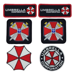May include: A collection of black, red, and white embroidered patches. The patches feature the text "UMBRELLA CORPORATION" and a red and white umbrella logo. Other patches include crossed swords, a shield, and a circular design.