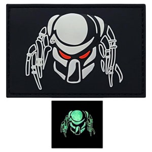 May include: A black patch with a white outline of a Predator's head with red eyes. The patch glows in the dark, as shown in the smaller image.