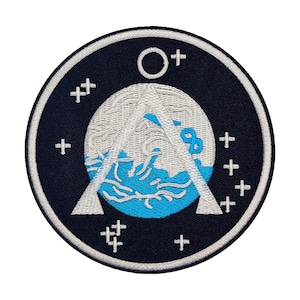 May include: A black and white embroidered patch with a blue and white design. The design features a circle with a white outline and a white crescent moon shape. The circle is filled with a blue and white wave pattern. The patch has a white border and is surrounded by white plus signs.