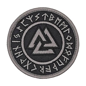 May include: A round, black patch with a gray border and a central design. The design features a gray Valknut symbol within a gray circle, surrounded by runic text. The patch is likely for clothing or accessories.