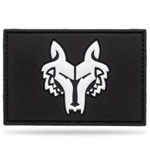 May include: A rectangular black patch featuring a stylized white wolf head graphic centered on the surface. The design is embossed with clean lines, showcasing a symmetrical wolf face with pointed ears and sharp features against a matte black background.