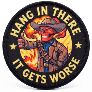 May include: A circular embroidered patch featuring a red skull wearing a cowboy hat and jacket, giving a thumbs up in front of an orange explosion. The black border contains the yellow text HANG IN THERE IT GETS WORSE with two yellow stars.