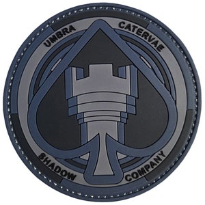 May include: A blue and gray embroidered patch with a stylized ace of spades design. The patch features a tower in the center and the text "UMBRA CATERVAE SHADOW COMPANY".