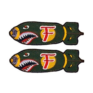 May include: Two green embroidered patches shaped like bombs with a shark tooth design and a red "F" in a yellow circle.