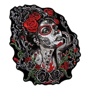 May include: Embroidered iron-on patch featuring a Day of the Dead-inspired woman with a sugar skull face, red roses, and black roses. The woman is wearing a floral crown and has green eyes.