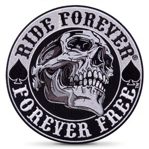May include: A circular embroidered patch featuring a central grey and white skull graphic. The black border contains the white text RIDE FOREVER at the top and FOREVER FREE at the bottom, with a black spade symbol on the left and right sides.