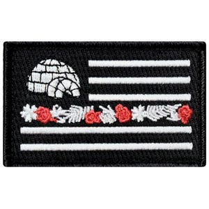 May include: Black and white embroidered patch with a white igloo in the top left corner. The patch features a white American flag with red flowers and leaves along the bottom edge.