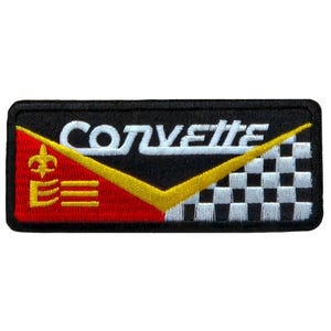 May include: A rectangular black patch with the word "Corvette" in white, a yellow chevron, and a checkered flag design. The left side features a red background with a gold crown and the letter "E".