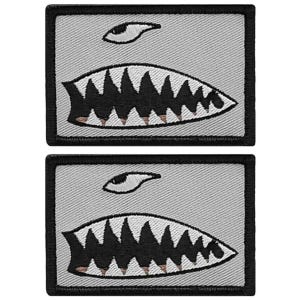May include: Two rectangular embroidered patches featuring a shark mouth design. Each patch has a gray background with a black border. The shark mouth is black with white teeth and a brown accent. Above the mouth is a stylized eye.
