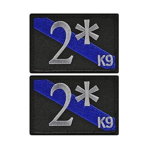 May include: Two black embroidered patches with a blue diagonal stripe, a white asterisk, and the number "2" in white. The text "K9" is also embroidered in white on each patch.