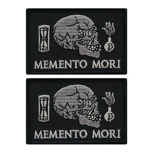 May include: Two black embroidered patches with a silver skull, hourglass, and bomb design. The text "Memento Mori" is embroidered below the design.