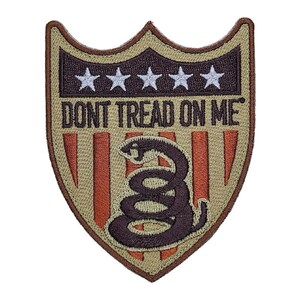 May include: A tan and brown embroidered patch with a shield shape. The shield has a red, white, and blue American flag design with a coiled snake and the text "DON'T TREAD ON ME".