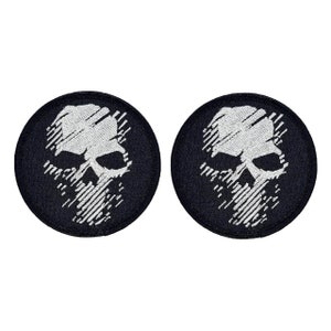 May include: Two black embroidered patches with a white skull design. The skull is stylized with a series of white lines.