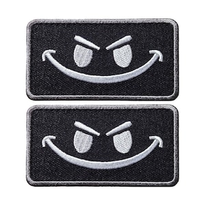 May include: Two black embroidered patches with a white smiling face with raised eyebrows. The patches are rectangular and have a white border.