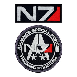May include: Two embroidered patches featuring the N7 logo from the Mass Effect video game series. The first patch is a rectangular black patch with white N7 lettering and a red stripe. The second patch is a circular black patch with a white N7 logo, three white stars, and the text "Alliance Special Forces Training Program" in white.