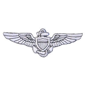 May include: White embroidered pilot wings patch with a shield in the center. The wings are spread out, with detailed feathering. The patch is designed to be sewn onto clothing or accessories. The patch is white with black stitching.