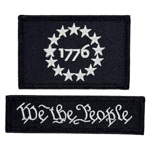 May include: Two black embroidered patches. The top patch features a circle of thirteen white stars surrounding the year "1776". The bottom patch features the phrase "We The People" in white cursive lettering.