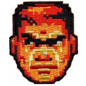 May include: A pixelated embroidered patch of a cartoon character with a red and orange face, black hair, and a black mustache. The character is wearing sunglasses.