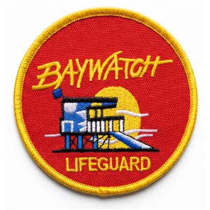 May include: A circular embroidered patch with a red background and a yellow border. It features the yellow text BAYWATCH above a blue and white lifeguard tower graphic set against a yellow sun. The word LIFEGUARD is printed in yellow below.