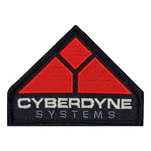 May include: A black and red embroidered patch with the text "CYBERDYNE SYSTEMS" in white. The patch features a stylized triangle design with three red triangles inside.
