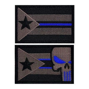 May include: Two embroidered patches, one with a black star and blue stripe on a gray and black Puerto Rican flag, the other with the same flag and a gray skull with blue eyes and stripes.