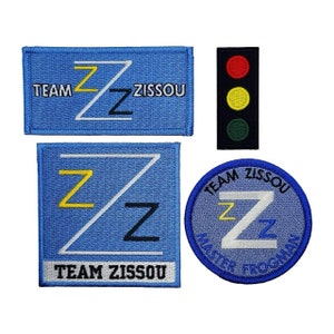 May include: Four embroidered patches featuring the text "Team Zissou" and a stylized letter "Z". One patch is a circle with a blue background, another is a rectangle with a light blue background, and the last two are rectangles with a light blue background. One of the rectangular patches has a traffic light design with red, yellow, and green lights.