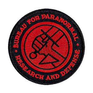 May include: Black and red embroidered patch with the text "Bureau for Paranormal Research and Defense" surrounding a stylized hand holding a sword.