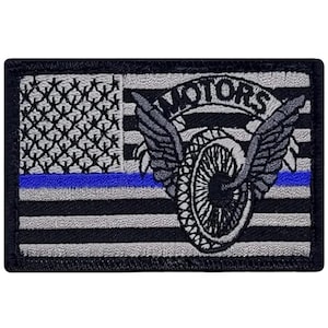 May include: Black and white embroidered patch with a motorcycle wheel with wings and the word "MOTORS" above it. The patch has a thin blue line across the bottom and a gray and white American flag design in the background.
