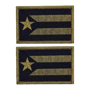 May include: Two embroidered patches featuring the flag of Puerto Rico. The patches are black with gold stripes and a gold star. The patches have a tan border.