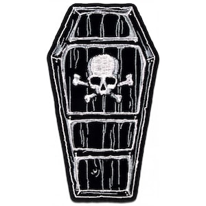 May include: A black and white embroidered patch shaped like a coffin. The design features a detailed white skull and crossbones centered within the coffin, which is outlined in white thread against a solid black background with vertical lines.