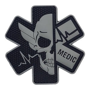 May include: Gray tactical patch with a skull and crossbones design. The skull is split in half, with a heartbeat graphic on one side and the word "MEDIC" on the other. The patch has a black honeycomb pattern.