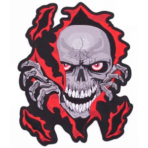 May include: An embroidered patch featuring a grey skull with cracked details, glowing red eyes, and sharp teeth, emerging from a torn red and black fabric background. The design includes skeletal hands reaching out from the jagged, ripped edges.