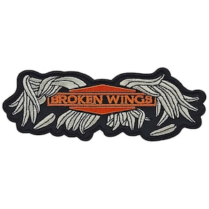 May include: A black and white embroidered patch with a pair of wings and an orange diamond-shaped banner with the text "BROKEN WINGS" in white.