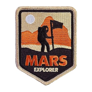 May include: A black and orange embroidered patch with a silhouette of a person standing on a mountain with a flag. The text "MARS EXPLORER" is below the image.