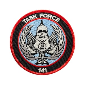 May include: A black and white embroidered patch with a skull and crossbones design. The patch has a red border and the text "TASK FORCE 141" in white.