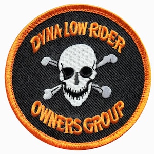 May include: Round black patch with orange trim and embroidered text. The patch features a white skull with crossed bones and the words "DYNA LOW RIDER OWNERS GROUP" in orange.