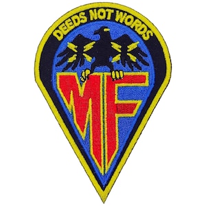 May include: A shield-shaped embroidered patch with a black border and yellow trim. It features a blue background, a black eagle with yellow lightning bolts on its wings, and the red letters MF. The text DEEDS NOT WORDS is in yellow.