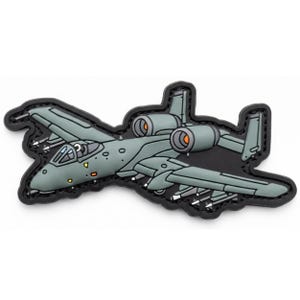 May include: A cartoon-style patch featuring a gray A-10 Thunderbolt II aircraft with orange engine details. The patch has a black border and includes details like missiles and a cockpit. The design is a stylized representation of a military aircraft.