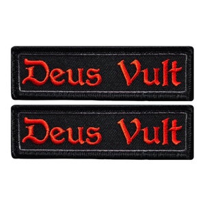 May include: Two black embroidered patches with the text "Deus Vult" in red lettering. The patches are rectangular and have a white border.