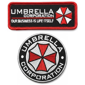 May include: Two embroidered patches featuring the Umbrella Corporation logo. One is rectangular with the text "UMBRELLA CORPORATION OUR BUSINESS IS LIFE ITSELF" and a red and white umbrella symbol. The other is a circular patch with the same logo.