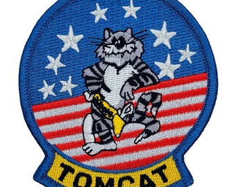May include: A blue and yellow embroidered patch with a cartoon cat wearing a yellow belt and a red, white, and blue American flag in the background. The text "TOMCAT" is written in yellow on a blue background.