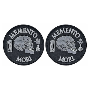May include: Two black embroidered patches with white stitching. Each patch features a skull, an hourglass, a flower, and the words "Memento Mori".