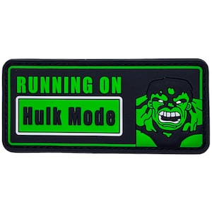 May include: A rectangular black and green patch featuring the text RUNNING ON HULK MODE in bold lettering. The design includes a graphic illustration of a green character with a fierce expression, clenched teeth, and dark hair on the right side.